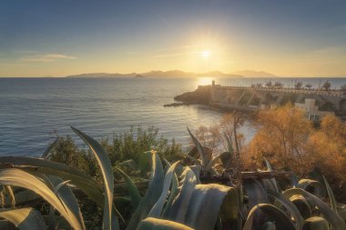 Piombino, gün batımında Piazza Bovio ve deniz fenerinin manzarası, arka planda Elba adası ve ön planda biraz bitki örtüsü. Maremma, Livorno ili, Toskana bölgesi, İtalya
