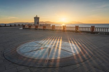 Piombino, Piazza Bovio 'nun rüzgar gülü manzarası ve günbatımında deniz feneri, arka planda Elba Adası. Maremma, Livorno ili, Toskana bölgesi, İtalya