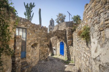 Blue door and bell tower view in a street of Bussana Vecchia. Ghost town in Sanremo, Liguria region, Italy. Abandoned due to an earthquake in 1887, today is a community of artists. clipart