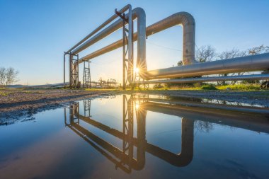 İtalya 'nın Tuscany bölgesindeki Larderello şehrinde gün batımında bir jeotermal enerji santralinin boru hatları ve yansıması. Jeotermal enerji bir alternatif ve sürdürülebilir enerji üretimidir..
