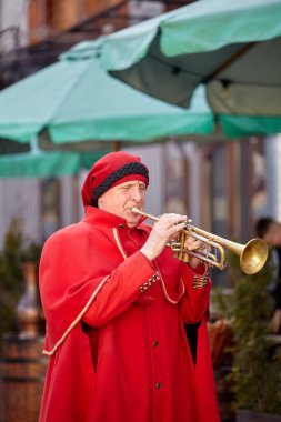 Lviv, Ukraine - 02.16.2021: Medieval trumpeter in red cloak. People in ancient authentic clothes of the 13th century.