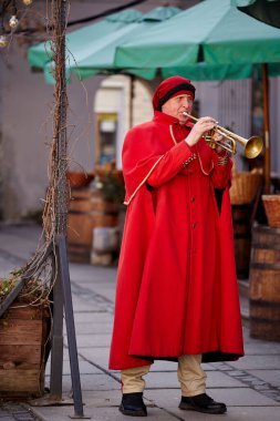 Lviv, Ukraine - 02.16.2021: Medieval trumpeter in red cloak. People in ancient authentic clothes of the 13th century.