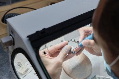 Dişçi el değirmeni diş kaplaması metal için 3D yazıcıda yaratıldı. Laboratuvardaki koruyucu kutuda seramik kaplamalarla çalışan diş teknisyeni. Metal işleme