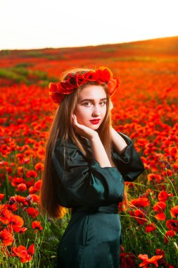 Tender girl with poppies in her hair. Happy teen girl portrait with wreath on head enjoying in poppy flowers nature background