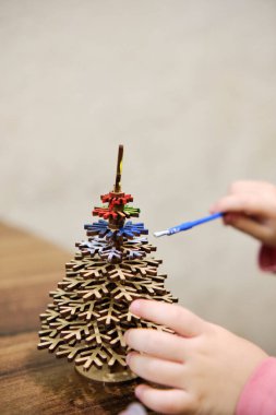 Küçük bir kız Noel ağacı şeklinde ahşap bir oyuncak çiziyor. O, her birine dikkatlice boya sürerek, konsantre bir şekilde başyapıtı üzerinde çalışır. Çocukların eğlencesi.