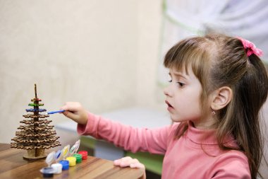 Küçük bir kız Noel ağacı şeklinde ahşap bir oyuncak çiziyor. O, her birine dikkatlice boya sürerek, konsantre bir şekilde başyapıtı üzerinde çalışır. Çocukların eğlencesi.