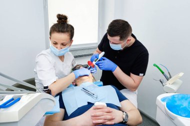 Diş İyileştirme Işığı: Polimerleşme Süreci. Dişçi ve asistan modern diş kliniğinde hastanın dişine dolgu yapıyor. Diş Hekimliğinde Takım Çalışması.