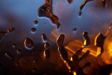 Su damlalarının soyut yakın plan çekimi ve yüzeydeki sıvı, altın ışığın ve serin mavi tonların bir oyununu yakalıyor. Soyut Sıvı: Altın Işık ve Mavi Yansımalar.