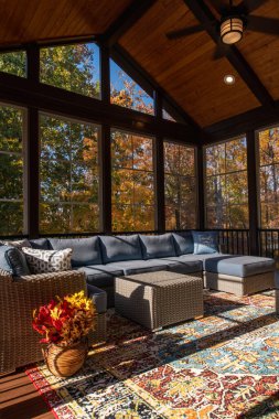 Cozy screened porch enclosure with contemporary furniture at Thanksgiving Holiday. Flower bouquet in a vase, autumn leaves and woods in the background. clipart