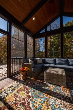 Şükran Günü 'nde modern mobilyalarla çevrili samimi sundurma. Veranda kapısı açık, vazoda çiçek buketi, sonbahar yaprakları ve arka planda orman..