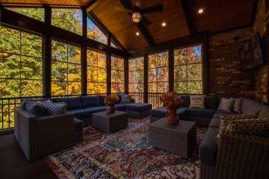 Şükran Günü 'nde modern mobilyalarla çevrili samimi sundurma. Vazoda çiçek buketi, sonbahar yaprakları ve arka planda orman..