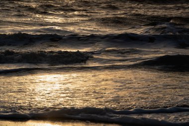 Güneş, okyanus suyunda ve sabahın erken saatlerinde ıslak kumda parlıyor..