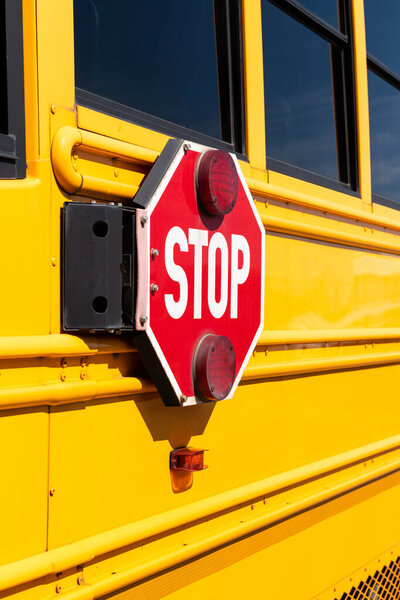 Red stop sign on the side of a yellow school bus.