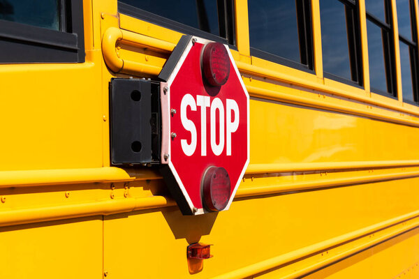 Red stop sign on the side of a yellow school bus.