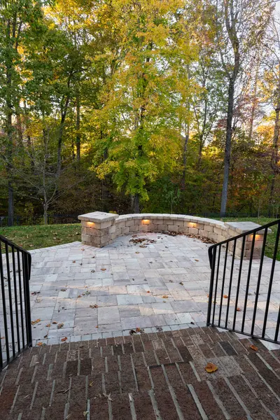 Picturesque backyard view in autumn season with patio pavers and stone wall, autumn leaves, and colorful woods in the background.