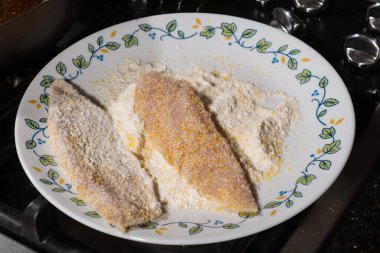 Tavada kızartılmaya hazır buğday ve mısır unu karışımıyla kaplı bir tabak balık filetosu. Ev yemeği konsepti.