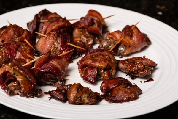 Cooked chicken liver wrapped with bacon. Roasted liver kebabs with on a white plate.