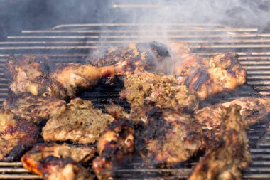Dumanlı bir barbeküde ızgara yapılan tavuk parçalarının yakın çekimi, yaz barbekü partileri ve barbekü temalı içerikler için mükemmel..