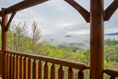 Dumanlı Dağlar 'ın üzerinde yuvarlanan güzel bir sis manzarası. Kabin güvertesinin ahşap sütunlarıyla çerçevelenmiş. Doğanın güzelliğine huzurlu bir kaçış.