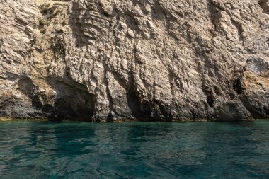 Yunanistan 'ın Zakynthos adası kıyı şeridi boyunca uzanan engebeli, ağaçlarla kaplı bir uçurumun yakınında, açık mavi gökyüzünün altında kristal berraklığında İyon Denizi suları var..