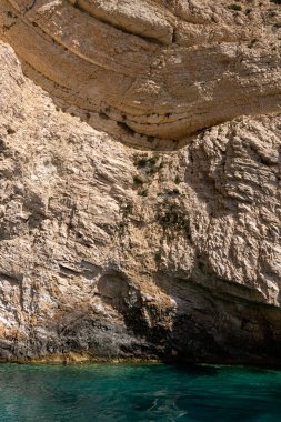 Yunanistan 'ın Zakynthos adası kıyı şeridi boyunca uzanan engebeli, ağaçlarla kaplı bir uçurumun yakınında, açık mavi gökyüzünün altında kristal berraklığında İyon Denizi suları var..