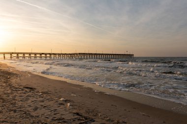 Oak Island İskelesi, Kuzey Carolina 'da parlayan gündoğumu gökyüzünün altında Atlantik Okyanusu' na doğru uzanırken dalgalar kıyı boyunca çarpar..