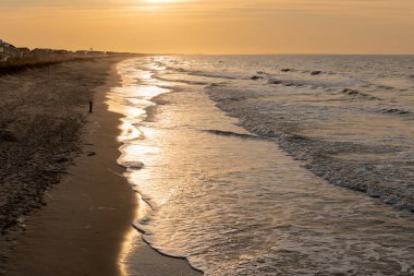 Altın sabah güneşi, Kuzey Carolina 'daki sessiz Oak Adası plajı boyunca hafif dalgalardan yansıyor..