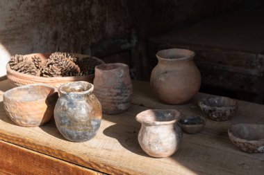 El yapımı kil kaplar ve çam kozalakları, Middleton Place, Charleston 'daki tarihi bir atölyenin içindeki ahşap bir masada yumuşak bir ışıkta otururlar..