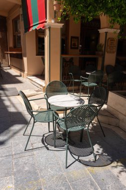 Yunanistan 'ın Zakynthos kentindeki sessiz bir ara sokağın gölgesinde metal kafe masası ve sandalyeler oturuyor.
