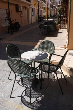 Yunanistan 'ın Zakynthos kentindeki sessiz bir ara sokağın gölgesinde metal kafe masası ve sandalyeler oturuyor.