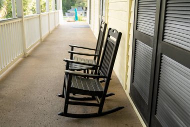 Siyah sallanan sandalyelerin yan görüntüsü verandanın duvarına dizilmiş, sıcak öğleden sonra ışığında yıkanmış..