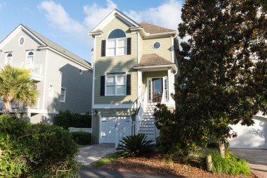 Palms Adası, Güney Carolina, ABD 30 Haziran 2025: Güneşli mavi gökyüzünün altında sakin bir yerleşim caddesi boyunca balkonları ve palmiye ağaçları olan pastel renkli kıyı evleri.