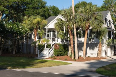 Palms Adası, Güney Carolina, ABD 30 Haziran 2025. Güneşli bir bahar öğleden sonrasında, Vahşi Kumlar Resort bölgesinde palmiye ağaçlarıyla çevrili beyaz, yükseltilmiş bir sahil evi..