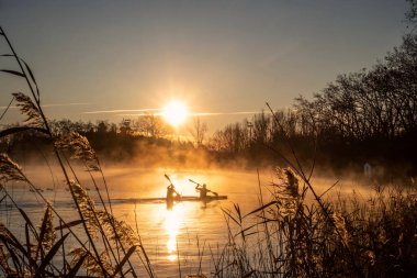 Banyoles Gölü 'nde kano eğitimi alan iki kişi, sabah güneşi.