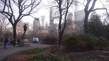 Çevresi ağaçlar ve Central Park 'taki insanlarla çevrili bir heykel. Sağdan Sola Görüntü