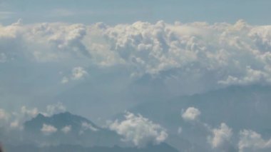 Bulutların ve dağ manzarasının üzerinden geçen uçak sağdan sola kayıyor.