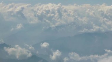 Dağ manzarasının üzerindeki bulutlar uçağın penceresinden süzülüyor sağdan sola kayıyor.