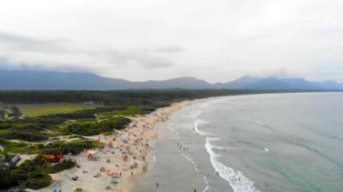 Floripa 'da bir kumsal manzarası, arkasında dağlar olan insanlarla dolu.