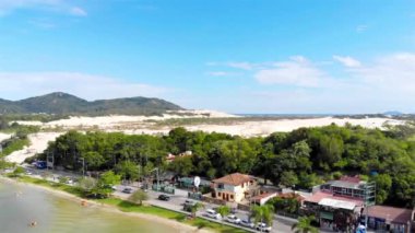 Arkasında yeşil dağlar ve deniz olan kum tepeciklerinin hava manzarası.