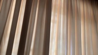 Büyük kapalı perdelerin arasından güneş parlıyor - soldan sağa doğru.