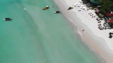 Deniz dalgalarının kıyı şeridine dokunuşunun drone görüntüsü kulübeler ve yeşilliklerle çevrili.