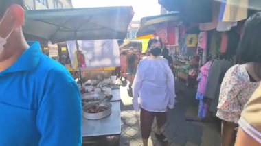 Kalabalık bir açık pazarda insanlar tezgahlardan alışveriş yapıyor.