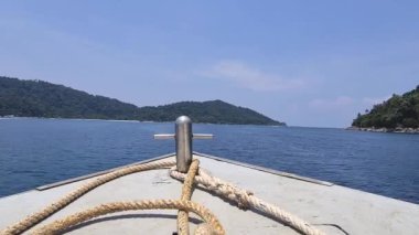 Yeşilliğin yakınındaki sakin denizde ilerleyen bir tekne.