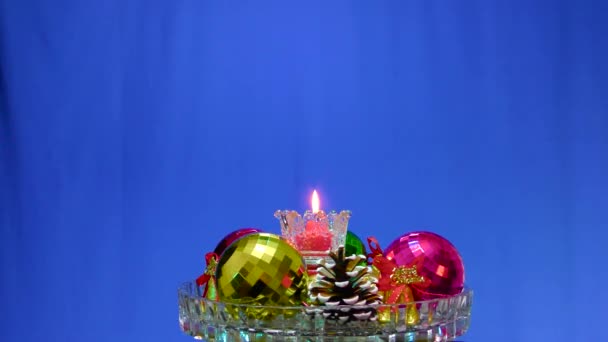 Синьому Фоні Скляній Поверхні Різдвяні Прикраси Навколо Палаючої Свічки — стокове відео