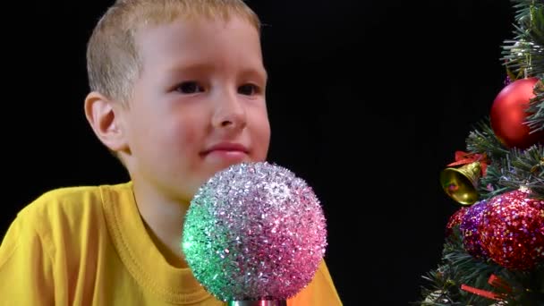 Niño Pequeño Examina Una Bola Plata Girando Cerca Árbol Navidad — Vídeo de stock