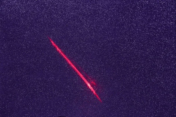 On a purple finely grained background, a short red beam of light