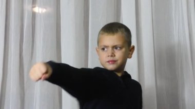 On a light background, an athlete in a black jacket trains punches