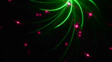 Siyah eğimli arkaplanda, rastgele çok renkli figürler ve yeşil ve pembe renkli ışınlar hareket ediyor.