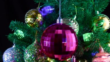 Koyu kırmızı bir Noel topu, toplarla süslenmiş Noel ağacı dallarının arka planında döner.