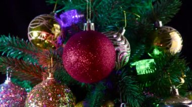Koyu kırmızı bir Noel balosu, Noel ağacı dalları ve toplarla süslenmiş çelenklere karşı döner.